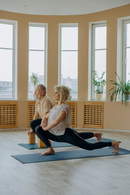 Elderly couple stretching in a yoga pose on mats indoors, focused on health and fitness.