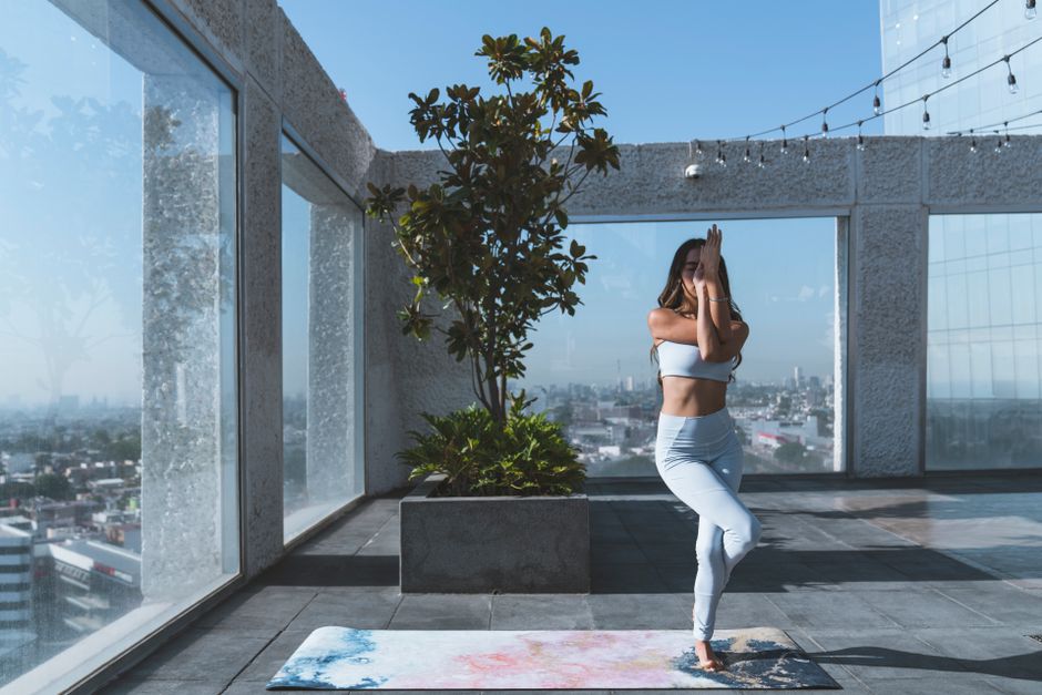 A woman engaged in yoga on a serene rooftop terrace with city views.