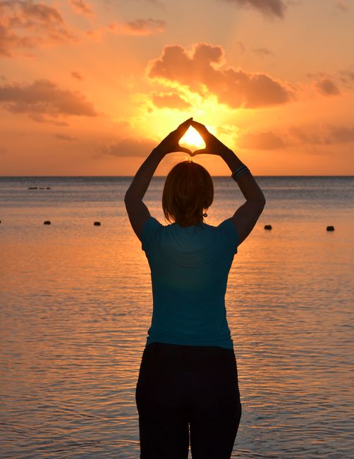 Woman in silhouette performing yoga pose by the ocean during a beautiful sunset.