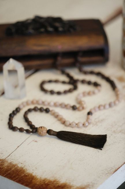 Close-up of handmade mala beads with tassel, made from natural stones and crystal, on wooden background.